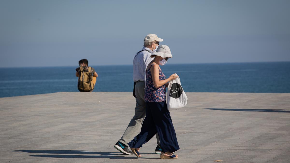 Dos personas con mascarilla pasean por el Paseo Marítimo de la Playa de la Barceloneta.