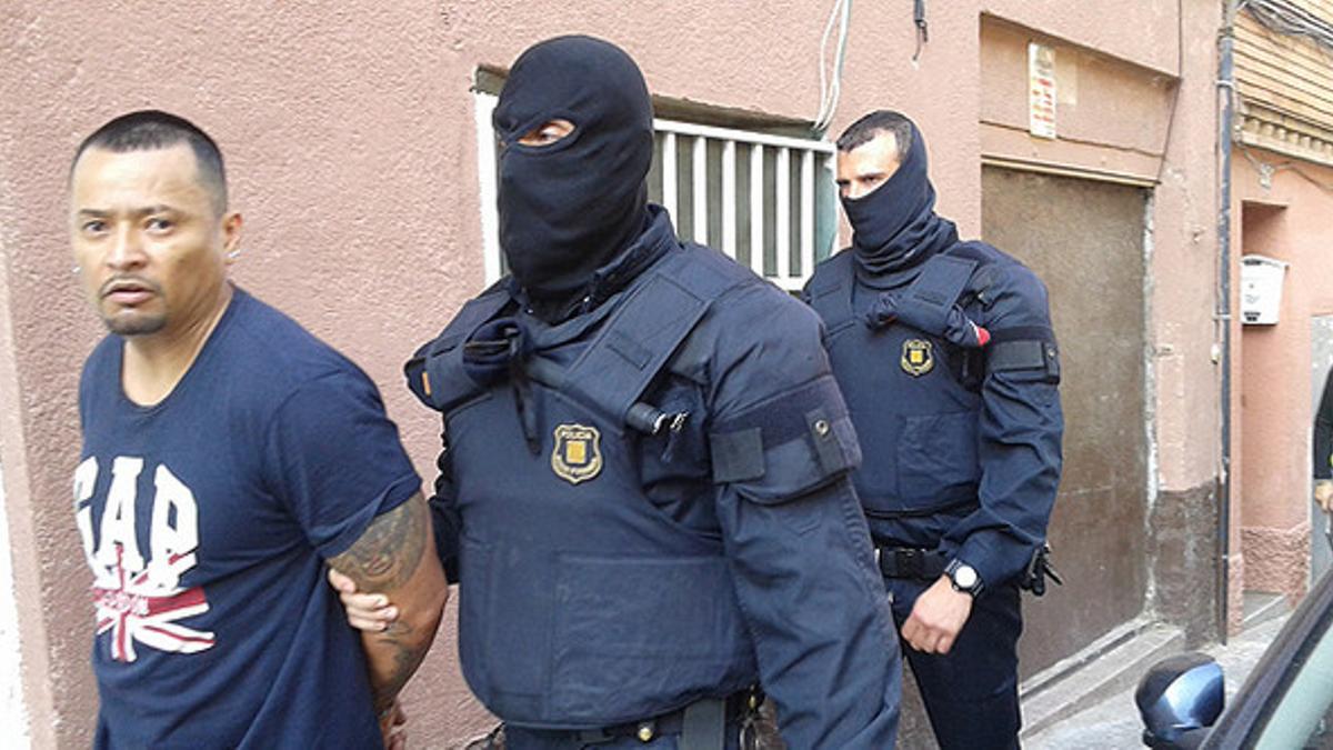 Dos agentes de los mossos se llevan detenido, en Santa Coloma de Gramenet, a uno de los presuntos miembros de la banda de Latin Kings desarticulada este miércoles.