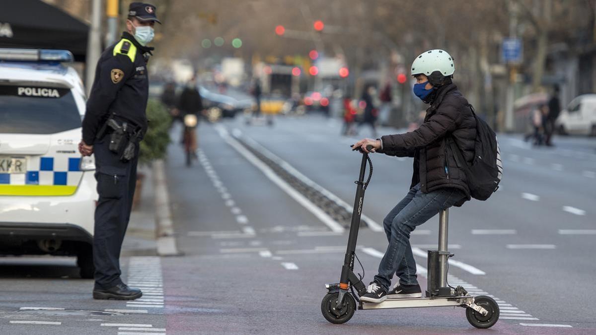 Un usuario del patinete eléctrico circula ante un guardia urbano, en Barcelona.