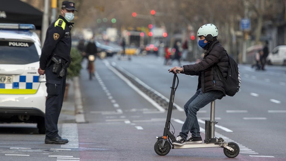 Un usuario del patinete eléctrico circula ante un guardia urbano, en Barcelona.