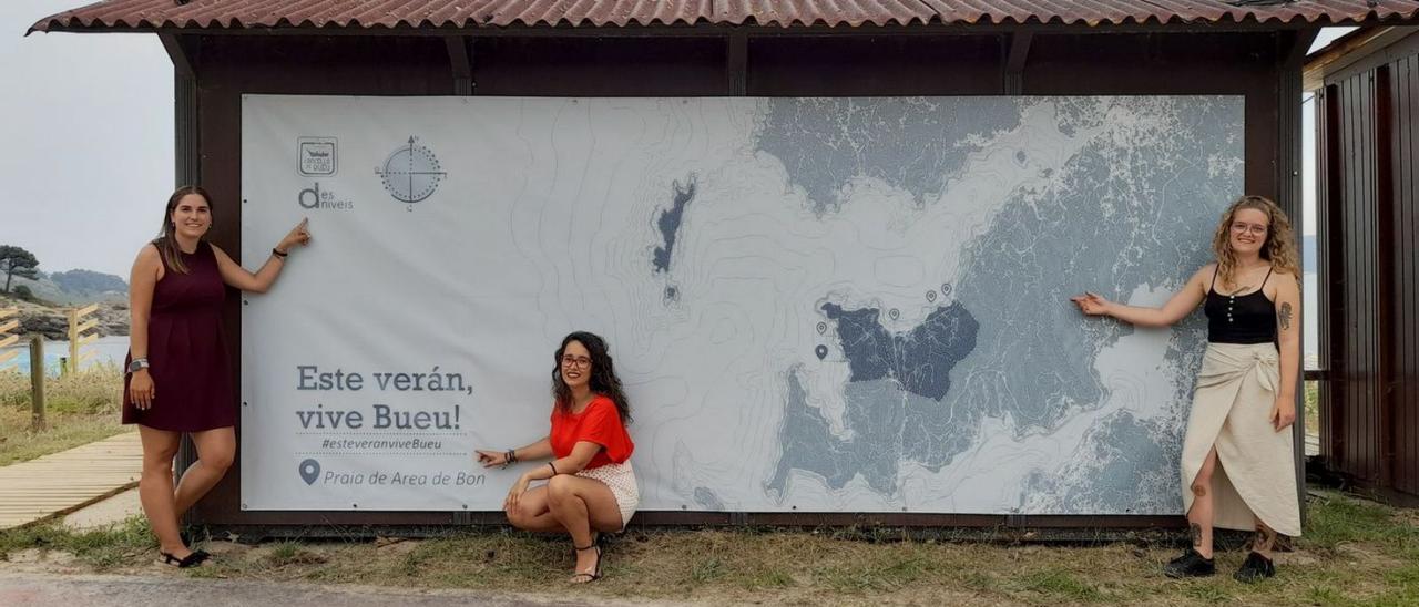 Silvia Carballo y dos de las arquitectas de Desniveis con el mapa instalado en la playa de Area de Bon.