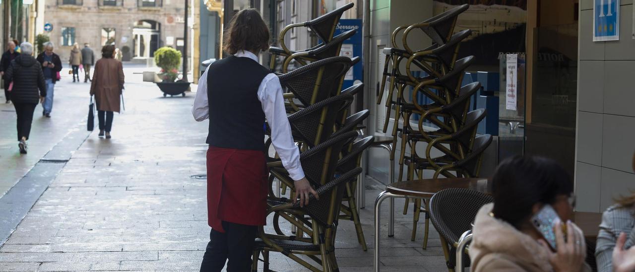 Una camarera coloca sillas en una terraza de Avilés.