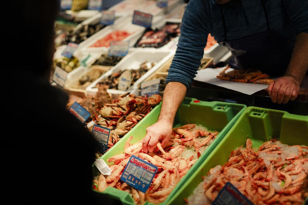 Un pescadero coge un puñado de langostinos de su expositor.