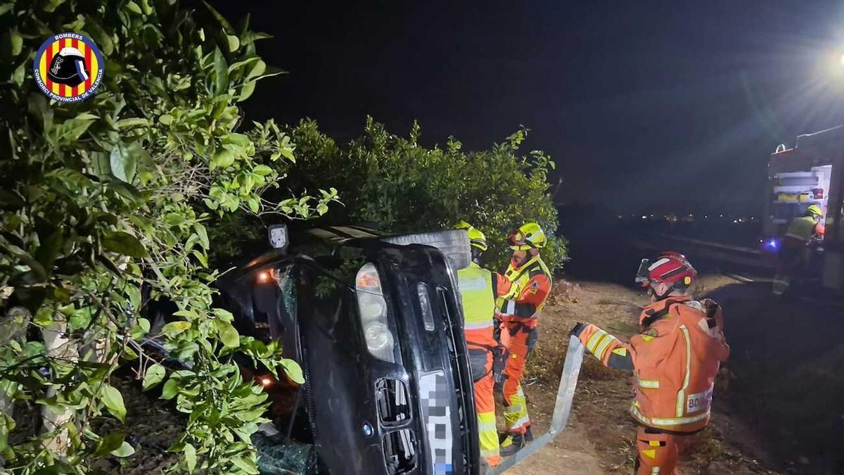 Los bomberos y el vehículo volcado, en el accidente de esta pasada madrugada en la CV-670 en Oliva