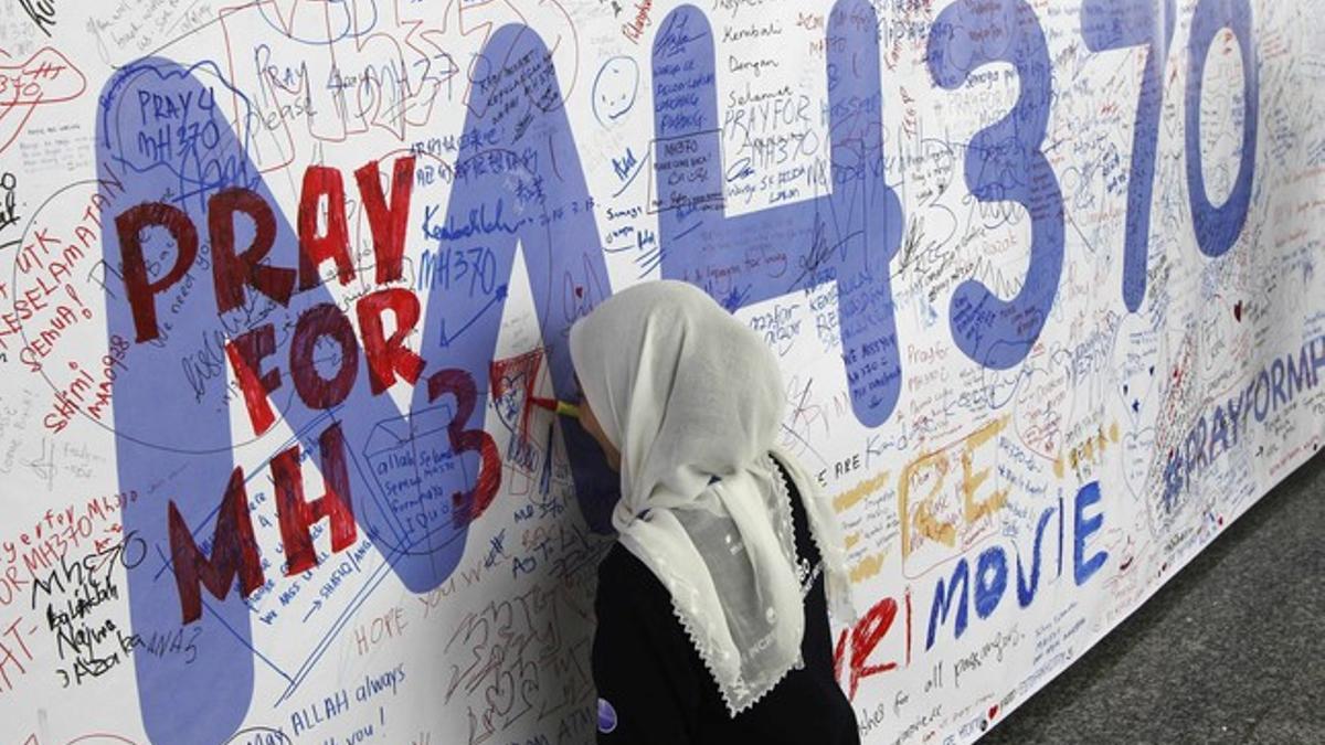 Una mujer escribe un mensaje en un muro dedicado al vuelo MH370 de Malaysia Airlines, este viernes en el aeropuerto de Kuala Lumpur.