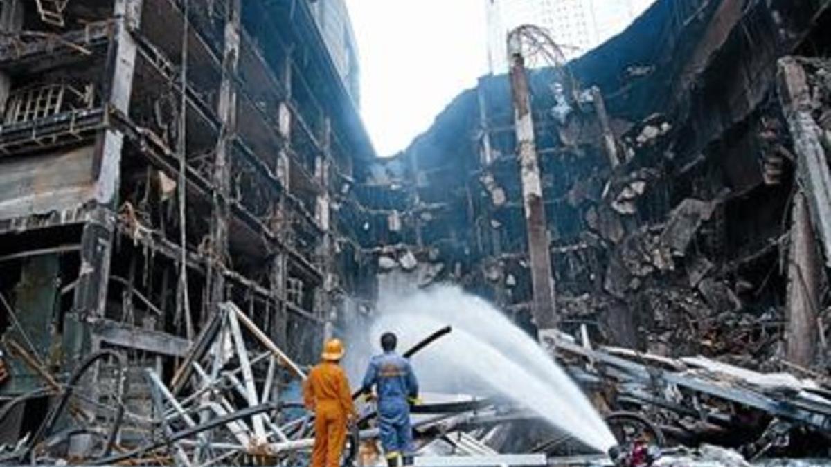 Unos bomberos rocían con agua las ruinas, aún humeantes, de un centro comercial incendiado en Bangkok.