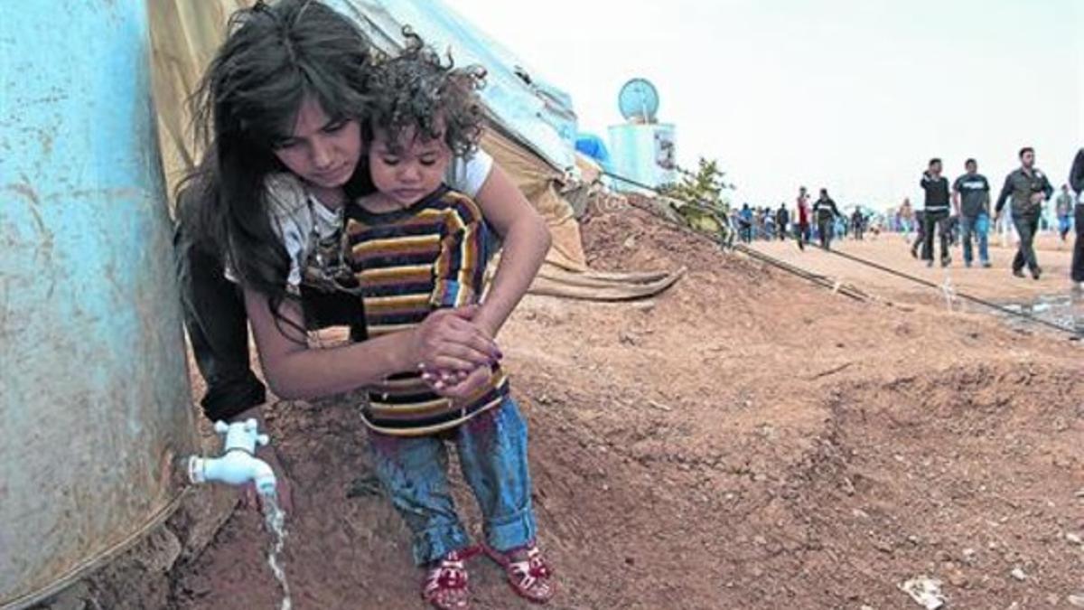 HIGIENE. Una chica lava las manos de su hermano menor, Safa, de 3 años, en el campo de refugiados sirios de Domiz (Irak).