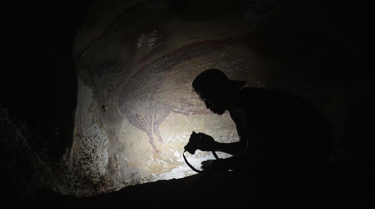 Un investigador trabaja frente a una de las pinturas descubiertas en la isla de Célebes, datadas en al menos 45.000 años.