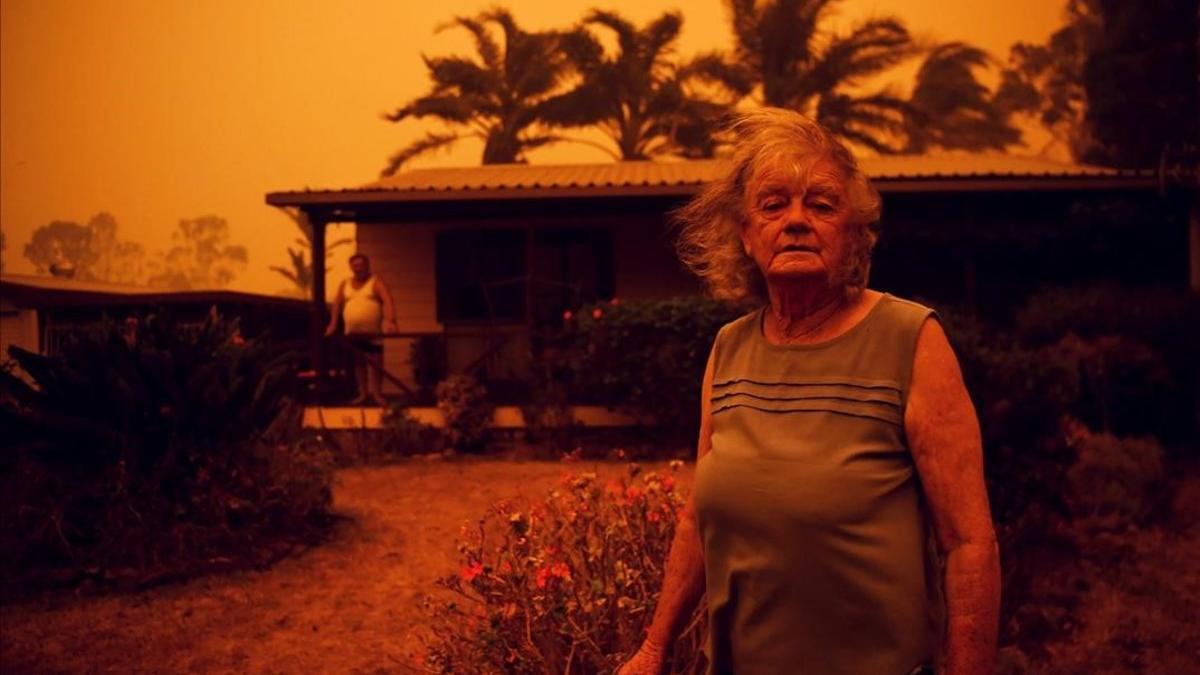 Una mujer mira a la cámara frente a su casa, azotada por los fuertes vientos que empujan el humo de los incendios en Nueva Gales del Sur, Australia
