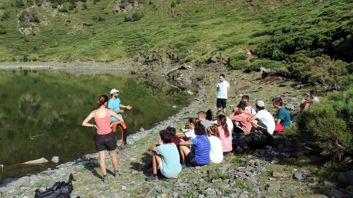 Un monitor dona explicacions a joves de colònies al costat d'un llac de muntanya.
