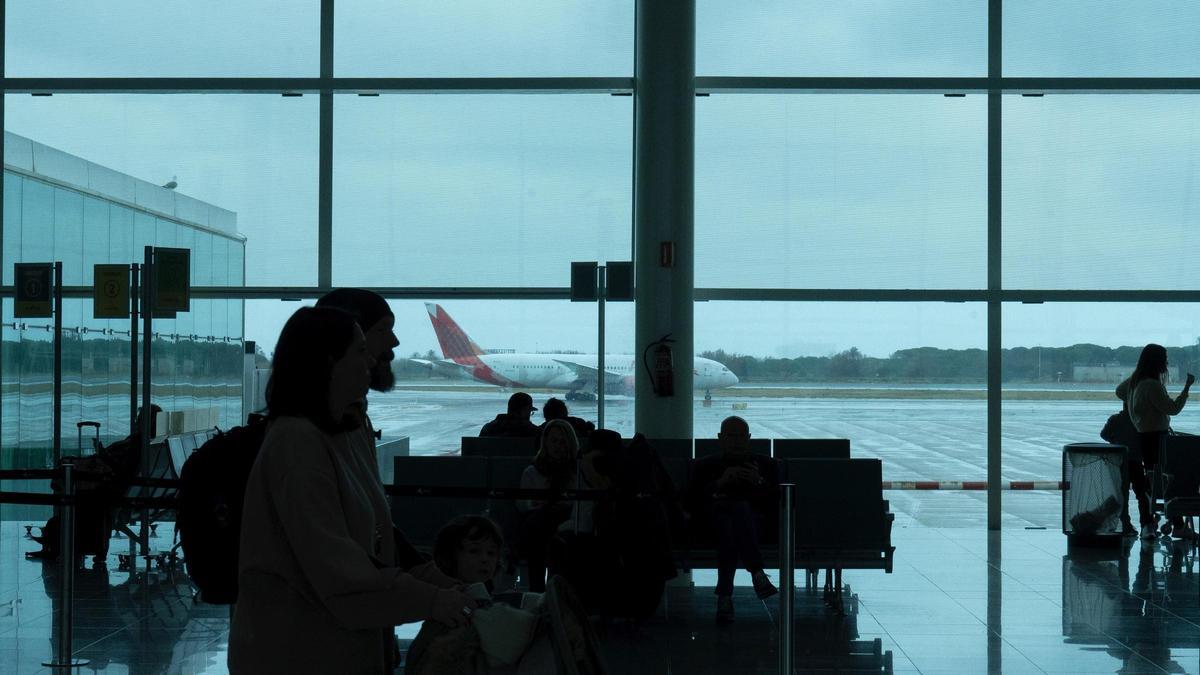 Varias personas esperan sentadas frente avion aparcado en una terminal de El Prat