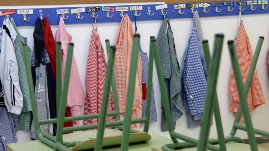 Renglera de bates penjades al penjador d&#039;una escola, amb totes les cadires de l&#039;aula cap per avall en primer pla