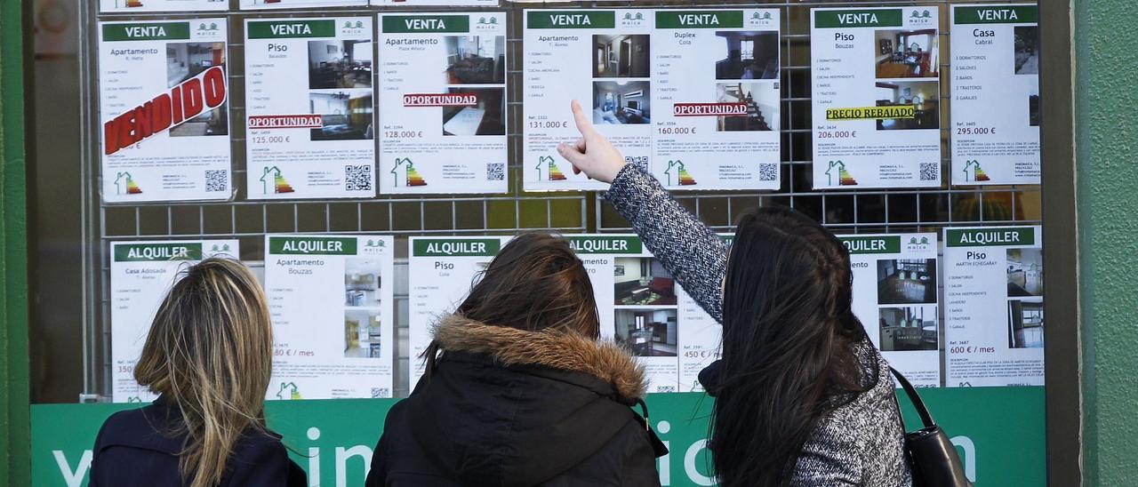 Tres jóvenes ven pisos de anuncios en una inmobiliaria de Vigo.