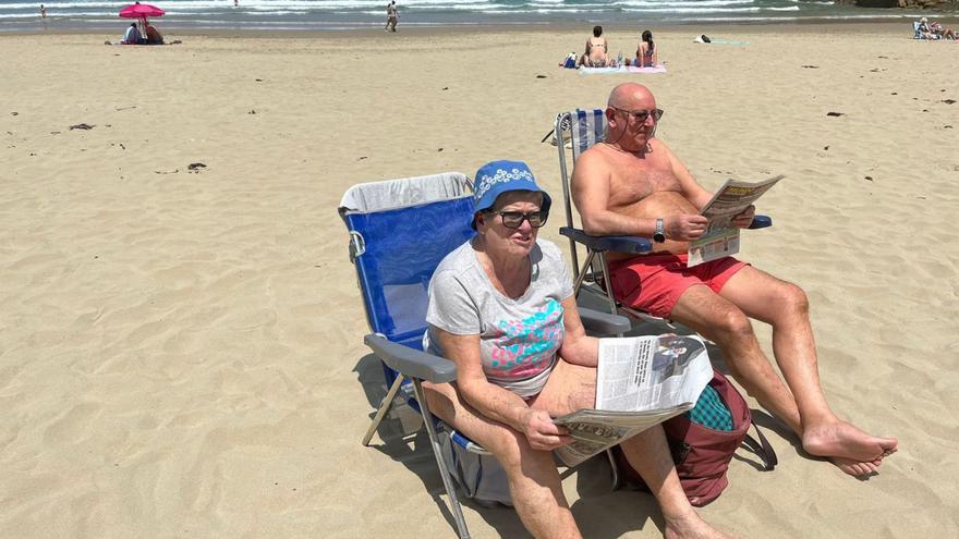 Paloma Alonso, leyendo LA NUEVA ESPAÑA, y Roberto Grana, ayer, en la playa de Aguilar. | LNE