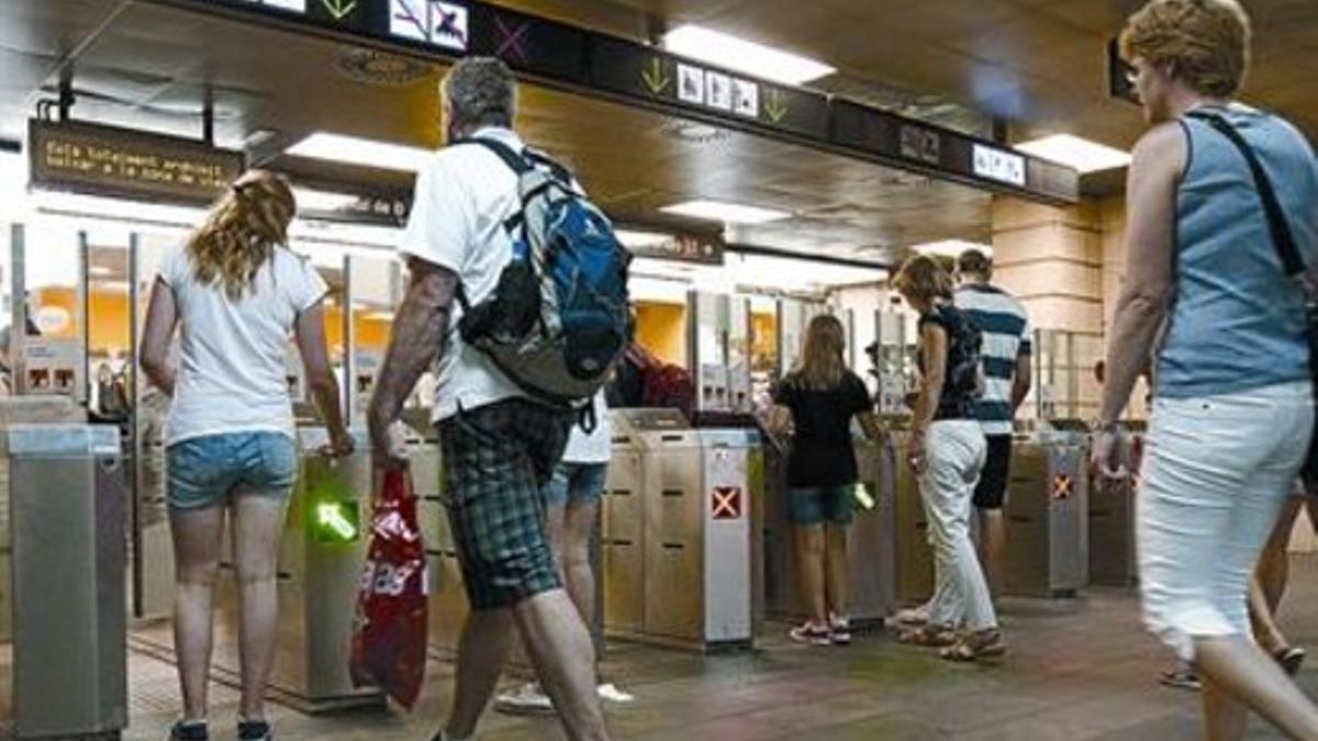 Varios viajeros validan sus tarjetas de transporte en la estación de metro de la plaza de Catalunya, en julio.