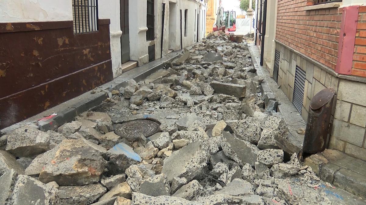 Al fondo, una máquina levanta el firme de la calzada en la calle Obispo Caballero de priego.