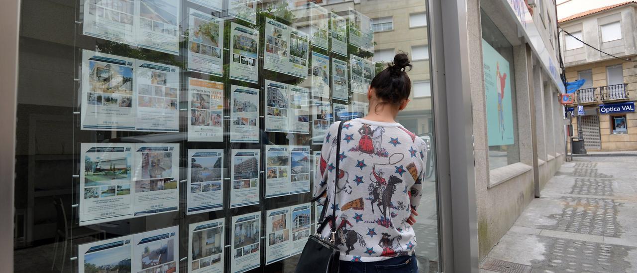 Una mujer mira el escaparate, lleno de ofertas, de una inmobiliaria.