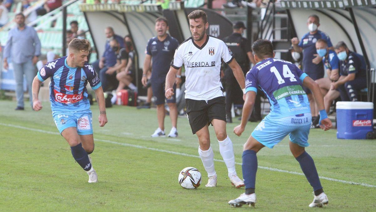 El delantero del Mérida Lolo Plá controla el balón entre dos jugadores del Coria, este domingo, en el Romano José Fouto.