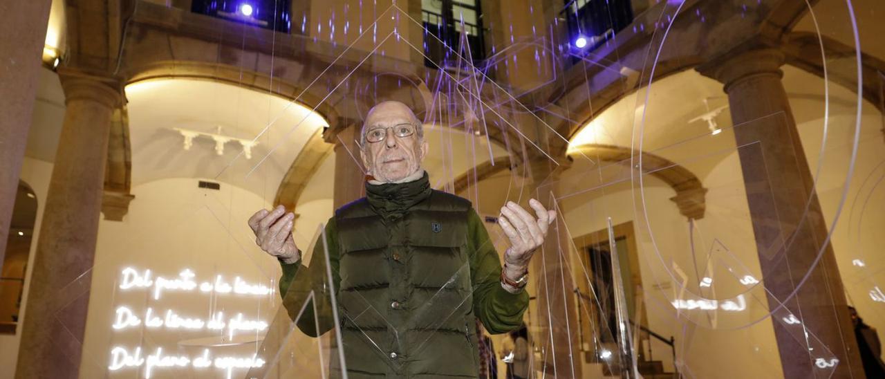 Arriba, Armando Pedrosa, entre las geometrías suspendidas en el patio del palacio de Velarde. A la izquierda, visitantes ante una de las esculturas en acero inoxidable del artista. Sobre estas líneas, una joven, junto a unas geometrías del artista en metal pintado colgadas como un lienzo. | Luisma Murias