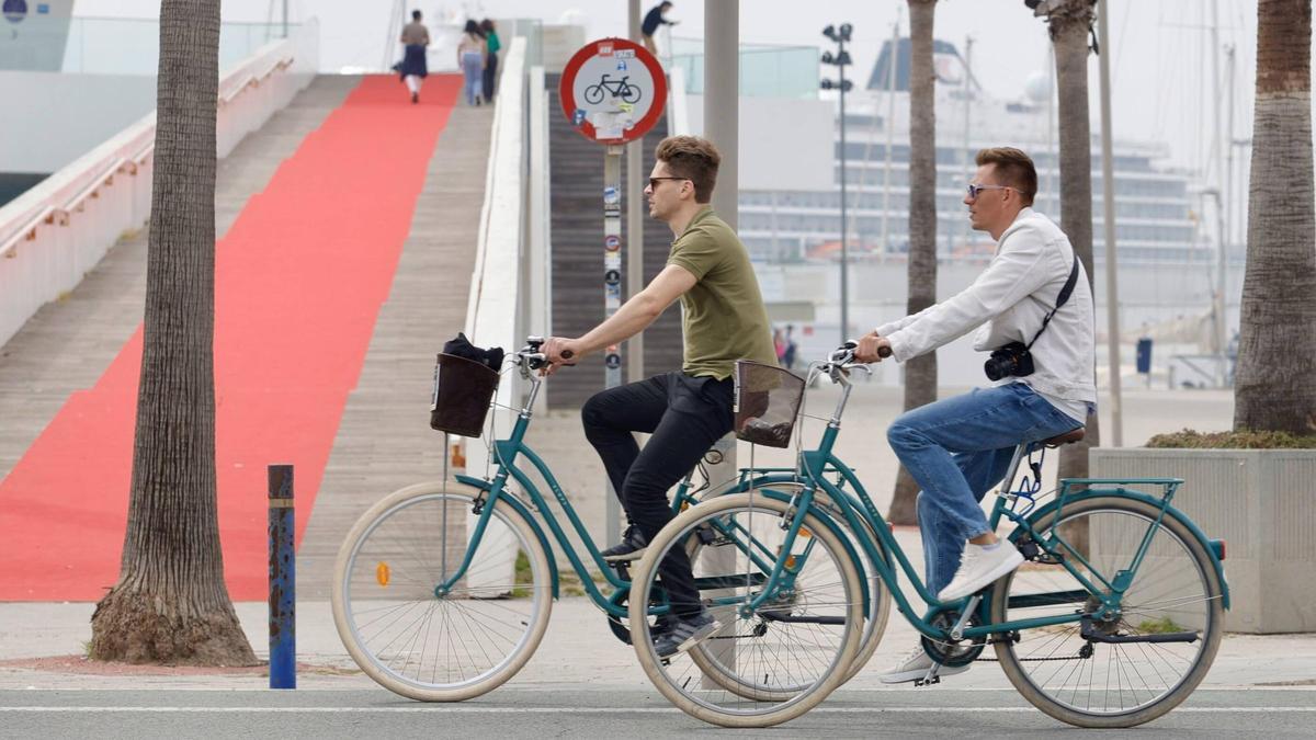 Dos turistas pasean en bicicleta por la Marina de València.