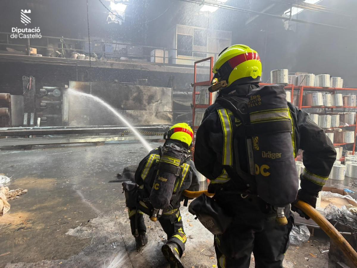 Los efectivos echan agua sobre la máquina incendiada este miércoles en una empresa de Nules.