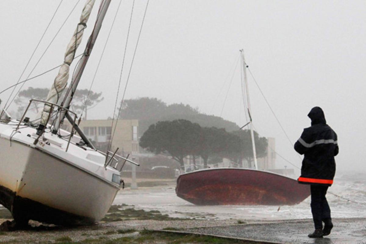 Un home observa diversos vaixells arrossegats a la platja per la tempesta que castiga la costa sud-oest de França.