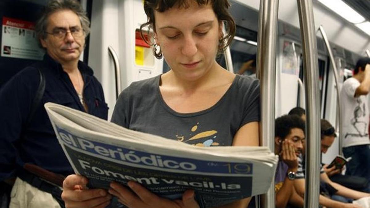 Una joven ojea un ejemplar de EL PERIÓDICO en el metro.