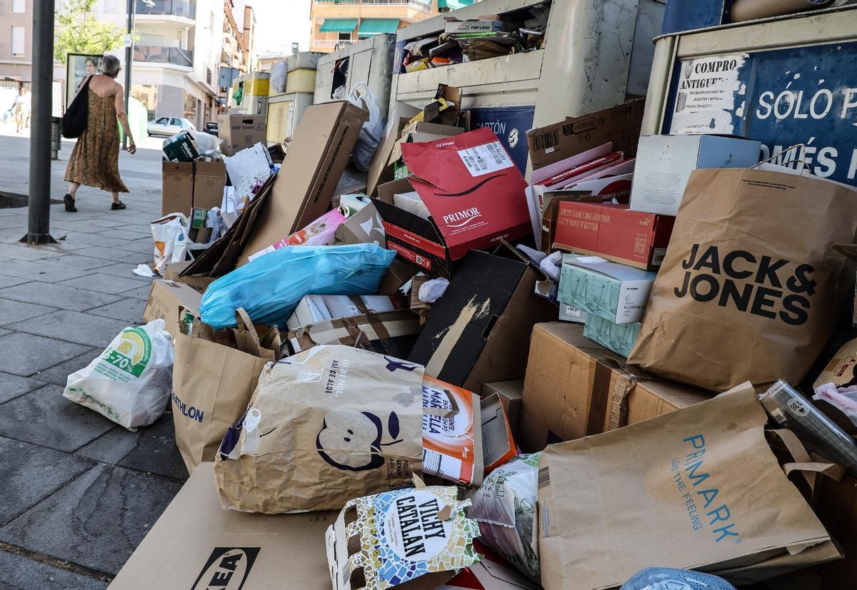 Restos de cartón y papel amontonados junto a varios contenedores en Ibi