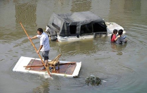 A man paddles a makeshift raft as residents walks past a partially submerged car on a flooded street in Yuyao