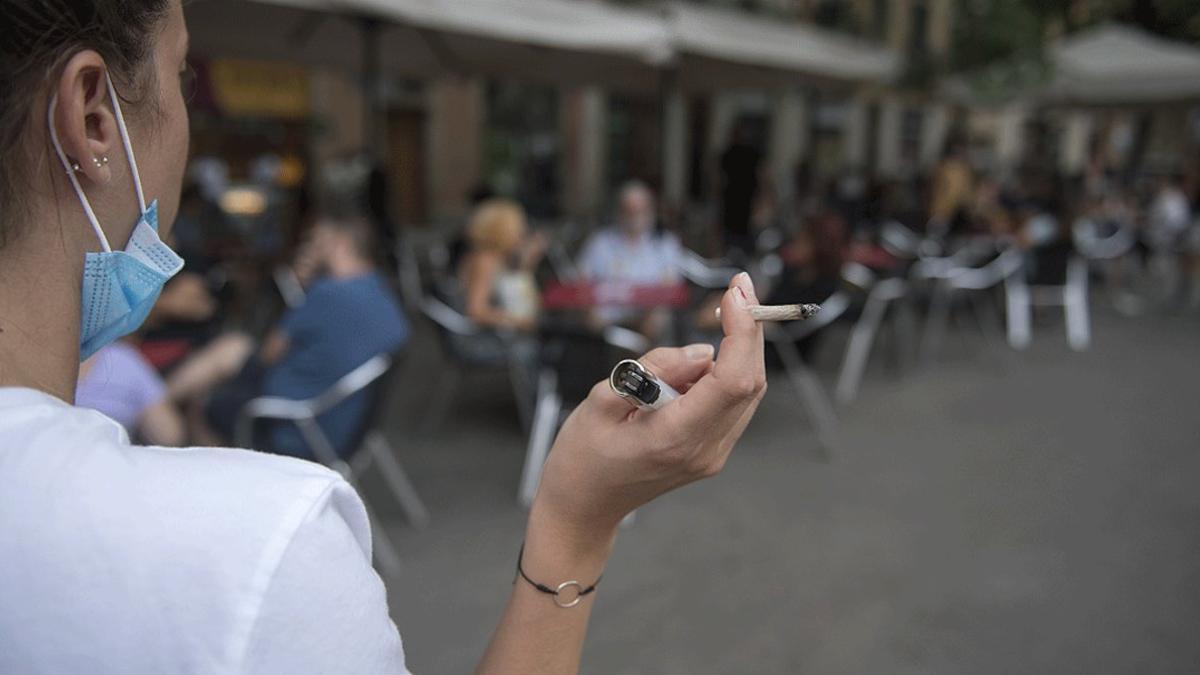 Una mujer fuma alejada de los clientes de una terraza de Barcelona, el pasado 18 de agosto