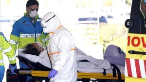 Una escena en la puerta del Hospital Puerta de Hierro de Madrid. El técnico de la ambulancia lleva un equipo de protección mínimo, en comparación con el del sanitario que recibe a la enferma.