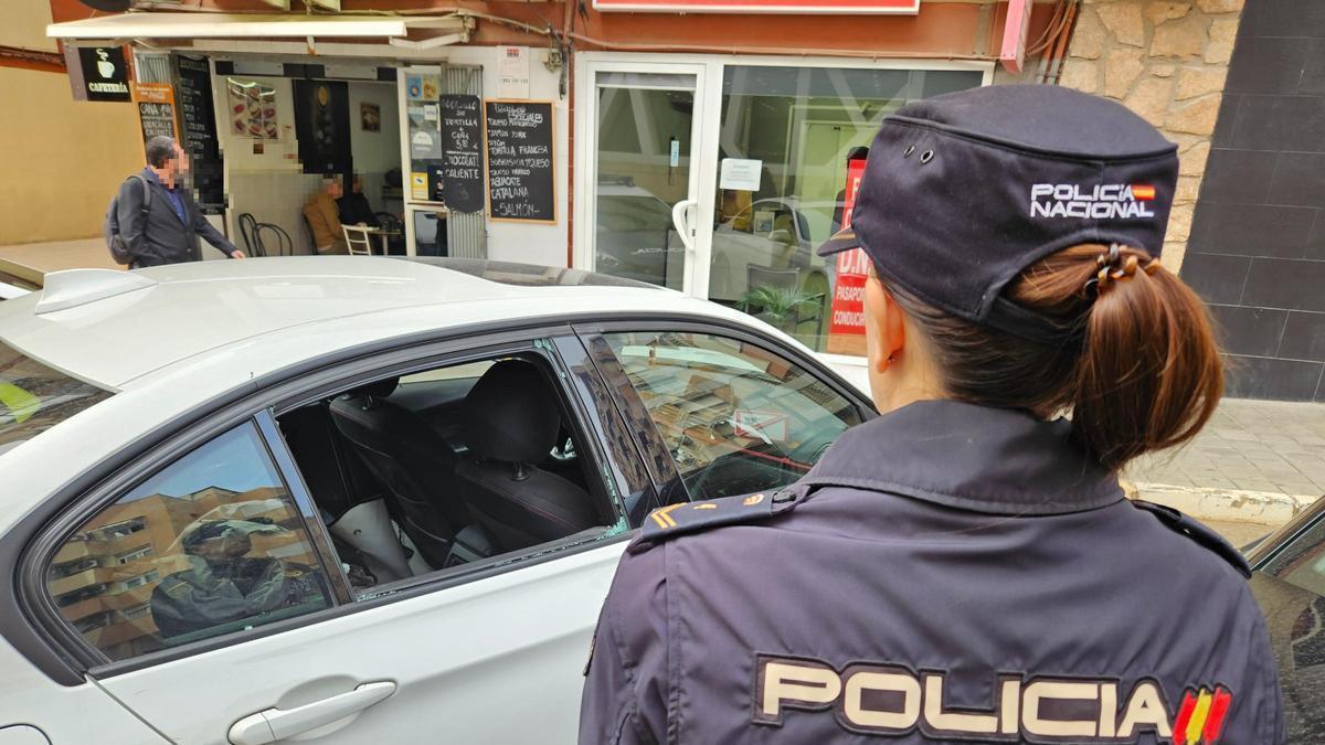 Una policía nacional frente a un coche con la ventanilla rota que ha sido inspeccionado en busca de huellas.