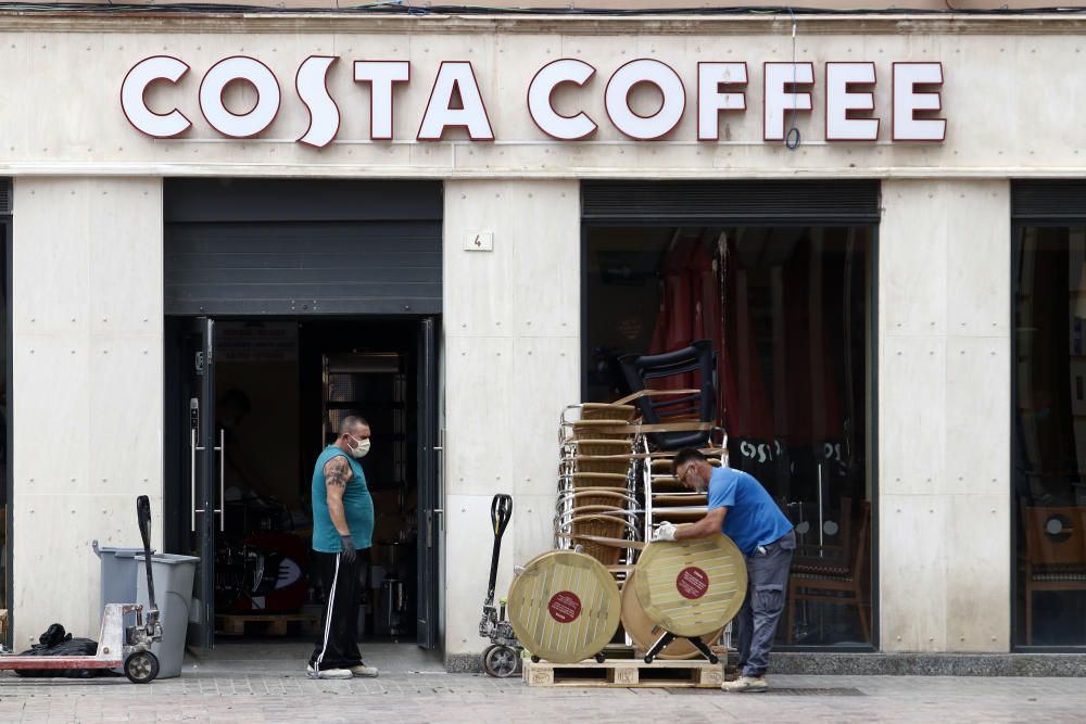 Imágenes de una lluviosa mañana de jueves en el centro de Málaga, donde al paisaje ya habitual de pocas personas y la mayoría de ellas con guantes y mascarillas se le han añadido los preparativos de bares, cafeterías y terrazas que se preparan para el inminente cambio de fase de la desescalada de la ciudad.