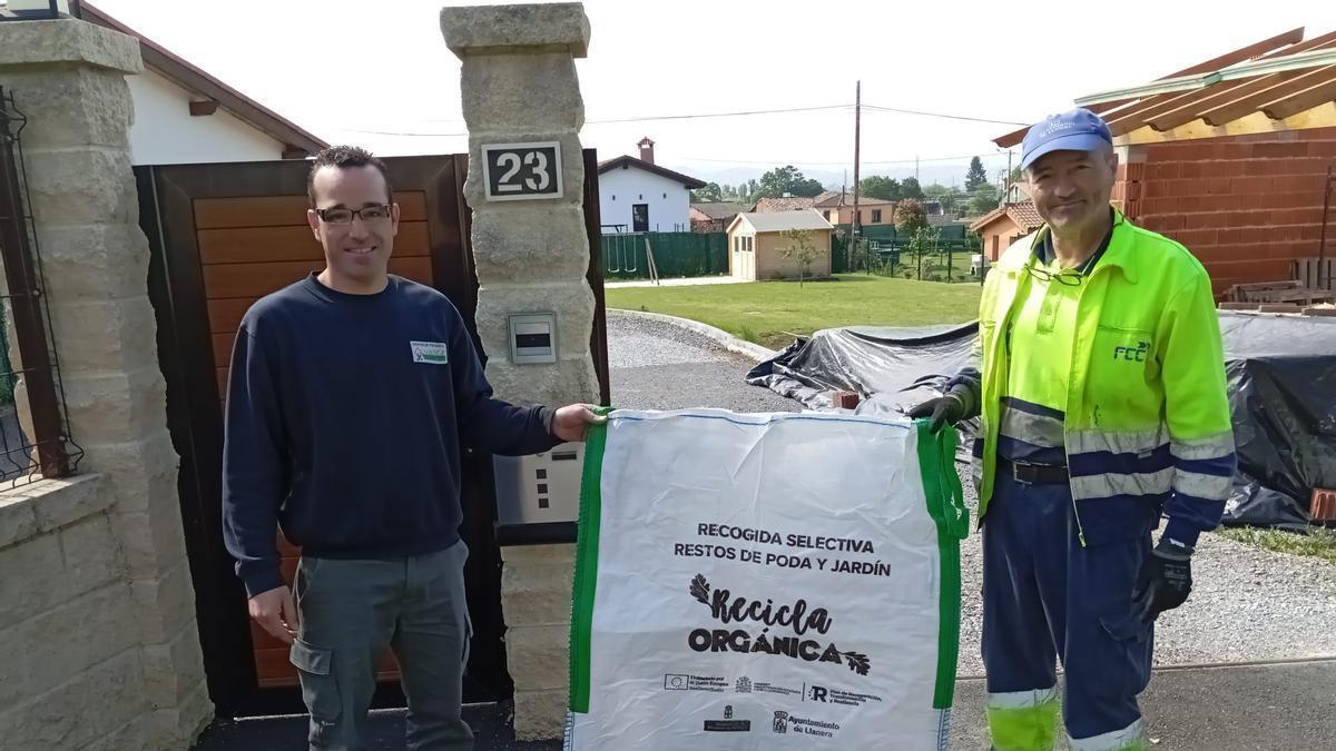 Por la izquierda, Manuel Antonio Álvarez, recibe una de las sacas reutilizables destinadas a la recogida de poda y siega de manos de Manuel Villar, operario de la empresa concesionaria del servicio