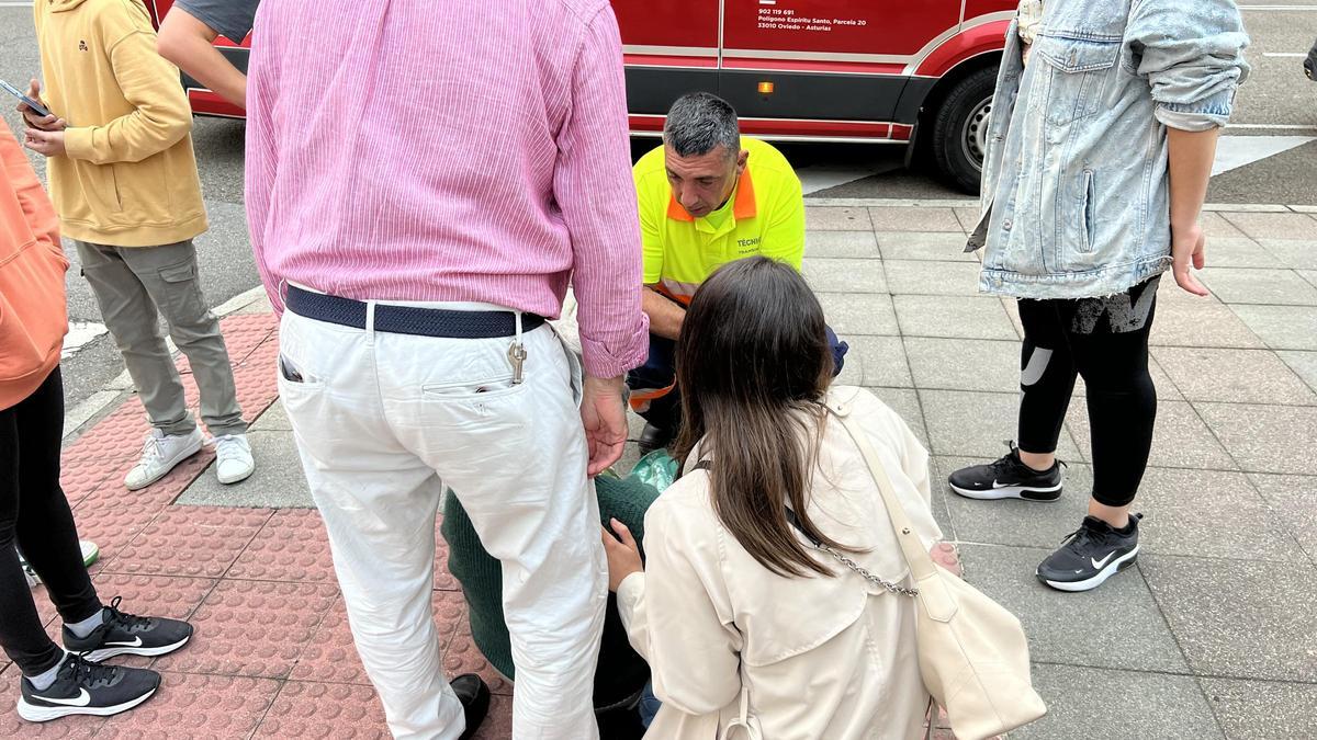 La mujer herida, sentada en el suelo, es atendida por un sanitario.