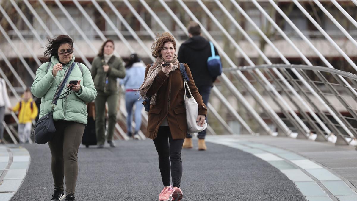 Peatones cruzan un puente con viento.