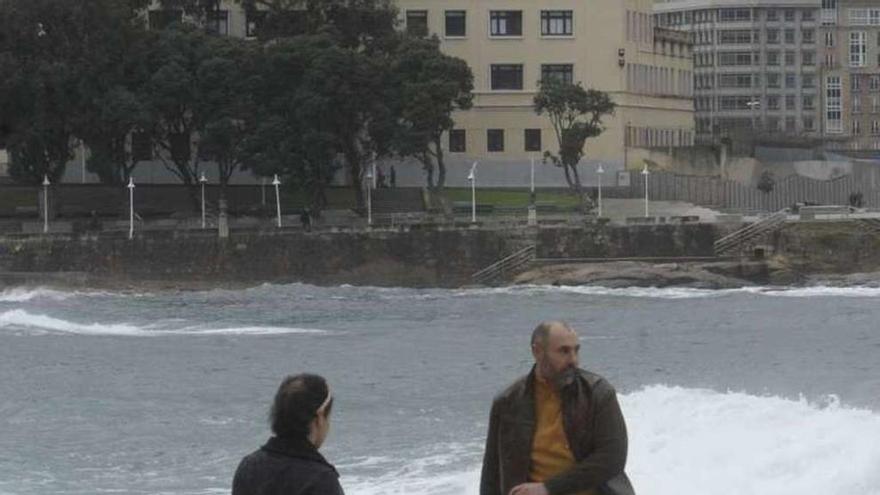 Dos personas pasean con un perro por la playa de Riazor.