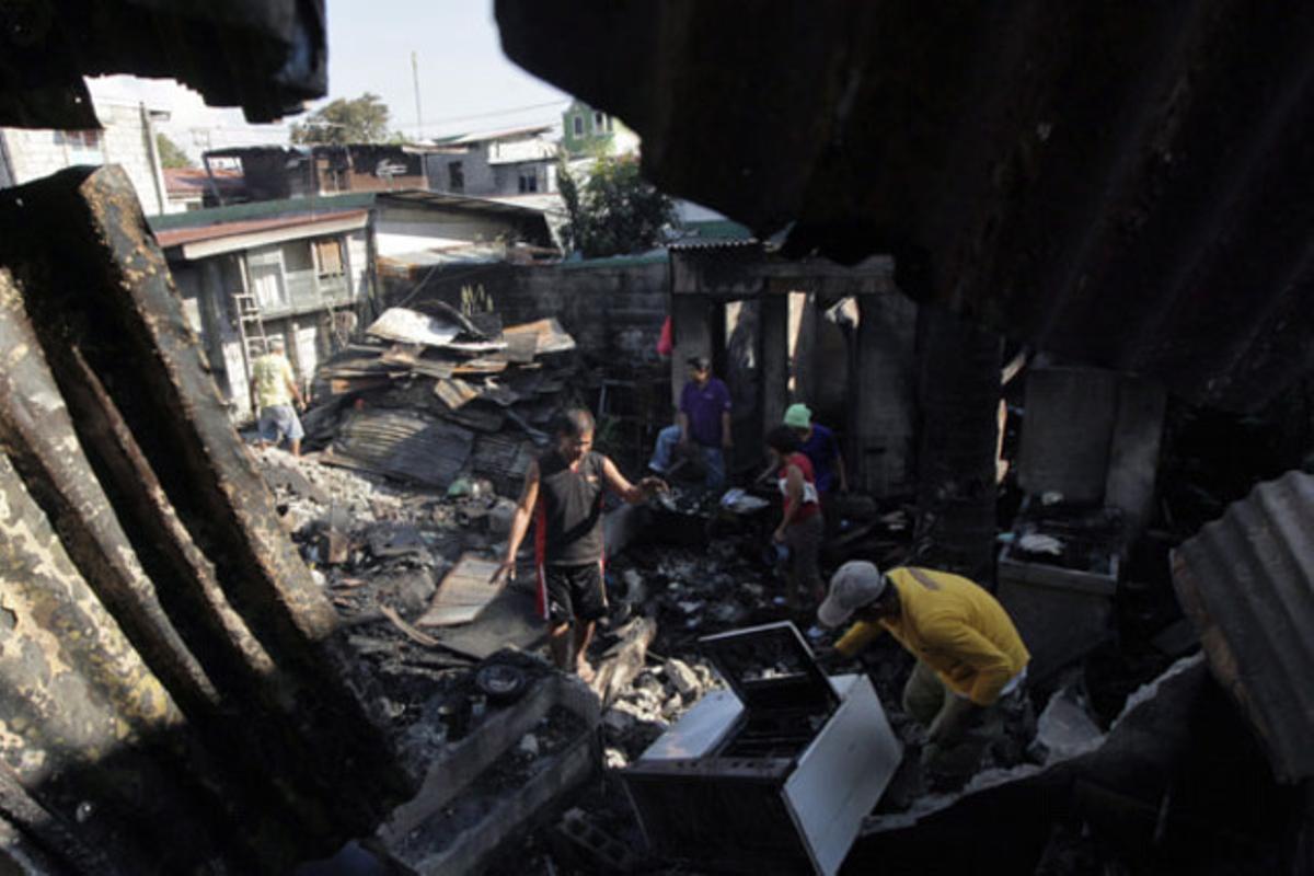 Uns homes busquen material servible entre la runa calcinada d’una vivenda en un barri de barraques a Caloocan, al nord de Manila (Filipines).