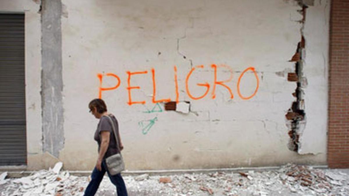 Una mujer pasa delante de la pared agrietada de un edificio en el que se ha escrito la palabra 'Peligro' con pintura roja.