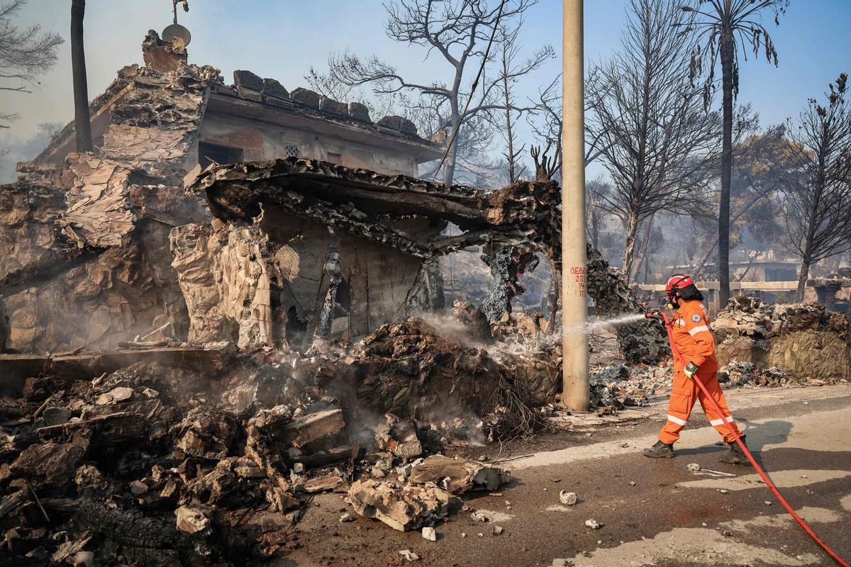 Un bombero rocía con agua una casa quemada tras un incendio forestal en la isla de Salamina, cerca de Atenas, el 16 de agosto de 2026