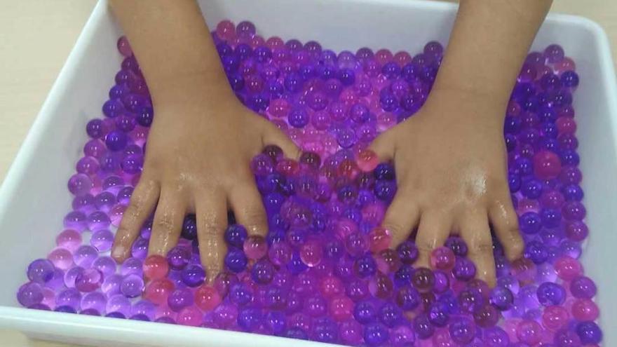 Un niño introduce las manos en un recipiente con bolas de gel de colores.