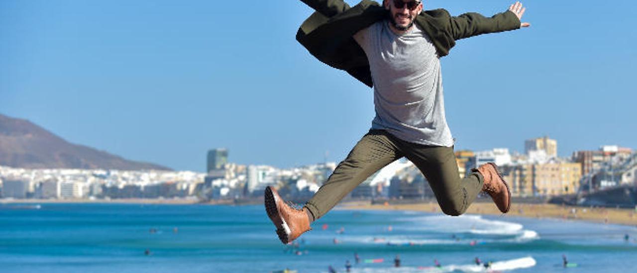 El bailarín, escritor y docente grancanario Quique Guijarro se suspende en el aire con un salto con la playa de Las Canteras y la ciudad de Las Palmas de Gran Canaria de fondo.