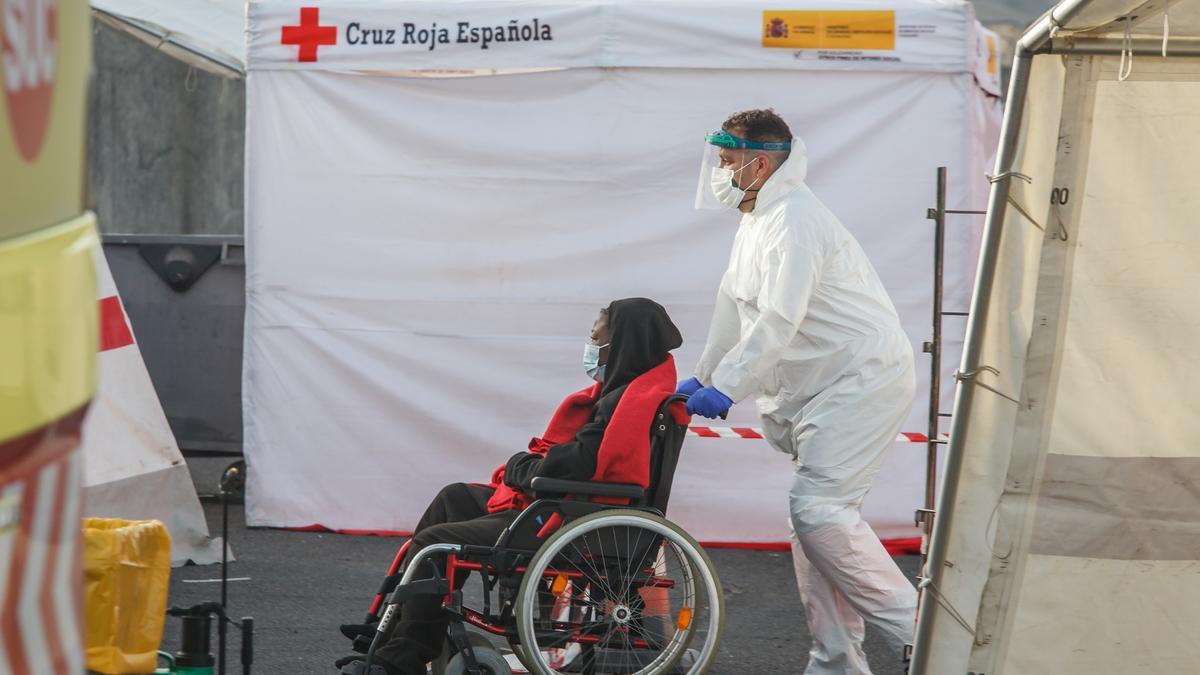 Archivo - Un trabajador lleva en silla de ruedas a una mujer rescatada por Salvamento cuando iba a bordo de una patera