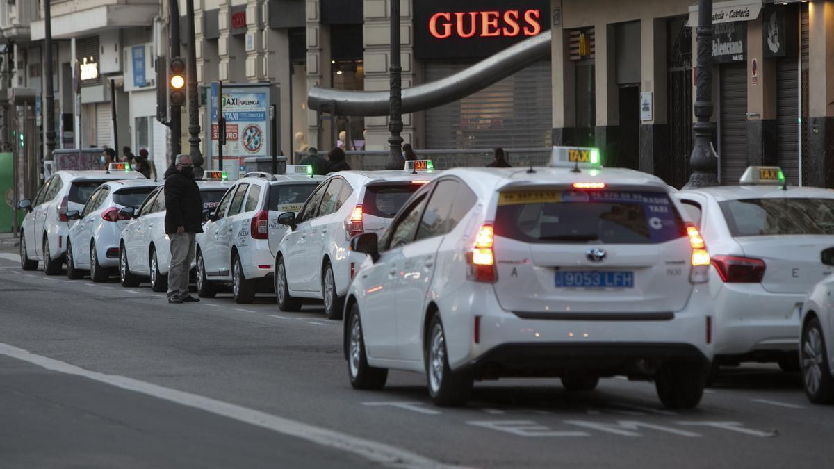 Varios taxis forman fila esperando clientes junto a una boca de metro de València.