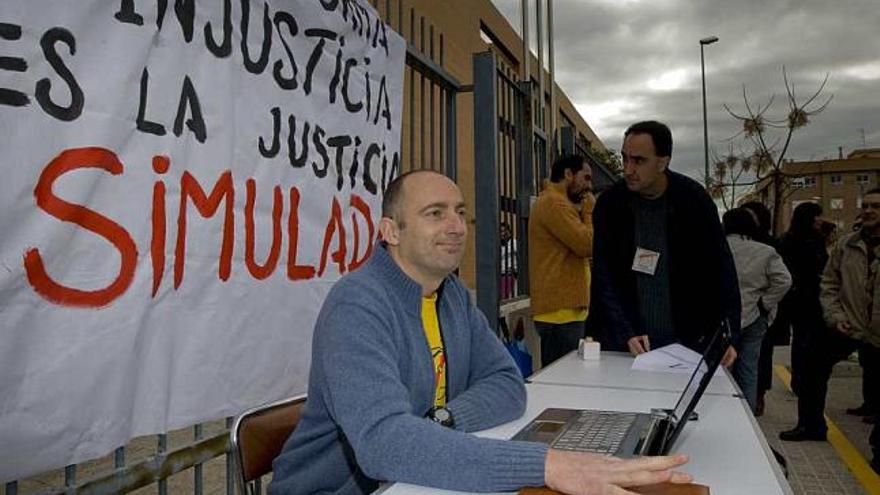 El director del IES Las Norias a las puertas del centro, con una mesa plegable, un portátil y el cartel de protesta detrás