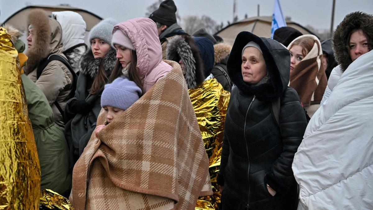 Refugiadas envueltas en mantas hacen fila bajo el frío mientras esperan ser trasladadas a una estación de tren después de cruzar la frontera de Ucrania hacia Polonia, en el cruce fronterizo de Medyka en Polonia, el 7 de marzo de 2022.