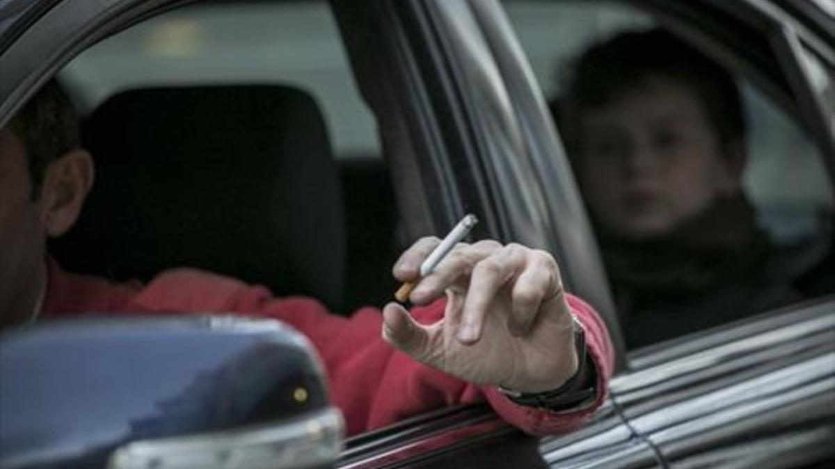 Un conductor fuma un cigarrillo en un coche, con un niño en el asiento de atrás.