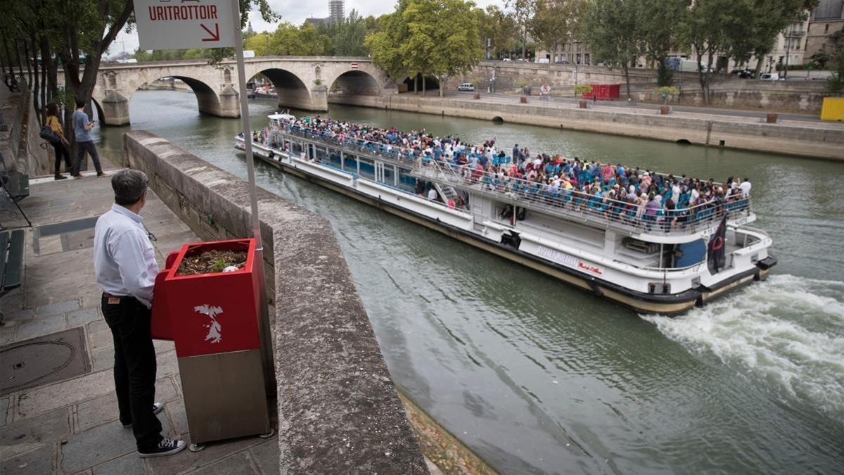 Un hombre utiliza un 'uritrottoir' ante el paso de un 'bateau mouche' en el Sena.