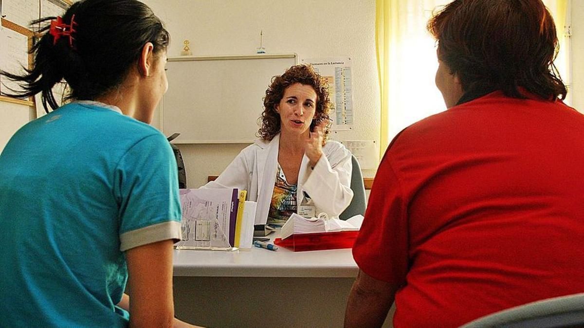 Una médico de familia atiende a dos pacientes en su consulta.