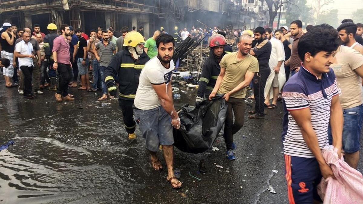 Bomberos y vecinos llevan el cuerpo sin vida de una de las víctimas del atentado en la barrio de Karada, en Bagdad.